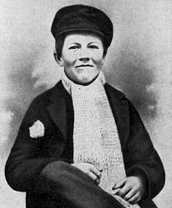 Slightly grainy black and white portrait of a stiff fourteen-year-old Edison in winter garb. A poorly patched area on the right shoulder leaks stuffing. He has a thick scarf and hat with his hands in his lap and right knee crossed over the left.