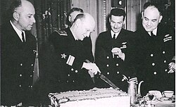 Rear Admiral Boris Dmitrievich Popov, commander of the 5th Independent Brigade of Soviet Navy Ships at Cold Bay, cuts a cake while his counterpart, Captain William S. Maxwell (right), commanding officer of U.S. Navy Detachment 3294, at Cold Bay, and overall commander of Project Hula, and members of their staffs look on during a party in Popov's honor on Memorial Day, 30 May 1945, probably at Dutch Harbor.[10]