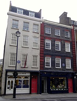 A color photograph of two adjacent buildings, the one on the left is white and the one on the right is dark brown.