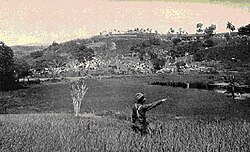 US Army photo taken near the base of Kettle Hill about July 4, 1898. The soldier is pointing up to the top of Kettle Hill. In the background are the block houses on San Juan Hill and the American encampment.