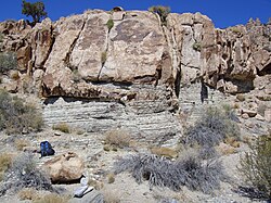 An intrusion (pink Notch Peak monzonite) inter-fingers (partly as a dike) with highly metamorphosed black-and-white-striped host rock (Cambrian carbonate rocks) near Notch Peak, House Range, Utah, United States