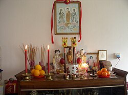 This picture was taken at a Malaysian Chinese home. This altar is dedicated to the three Pure Land sages, Avalokitesvara, and Sathya Sai Baba. On the left of the altar is a glass filled with rice. Joss sticks are stuck into it after the ancestors are invited to partake in the offering of food specially prepared for them on the Hungry Ghost festival prayers.