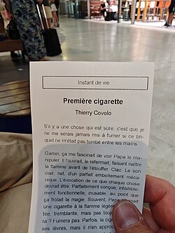 Person holding a small printed French short story booklet titled "Première cigarette" in a public space