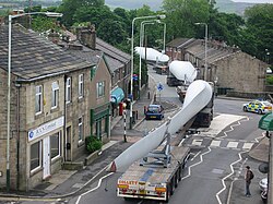 A turbine blade convoy passing through Edenfield in the U.K. (2008). Even longer 2-piece blades are now manufactured, and then assembled on-site to reduce difficulties in transportation.