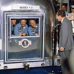 President Nixon visits the Apollo 11 astronauts in quarantine after observing their landing in the ocean from the deck of the aircraft carrier USS Hornet.[35]
