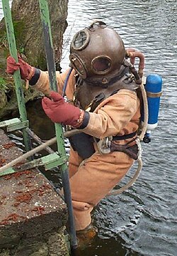 Helmeted diver entering the water. He has a back mounted Draeger DM40 rebreather system in addition to the surface supply air hose