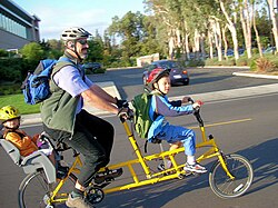 A man rides a multi-seated bicycle with two children (2007). In most developed countries, except France, parents have been spending more time with their children than in the past.[367][368]