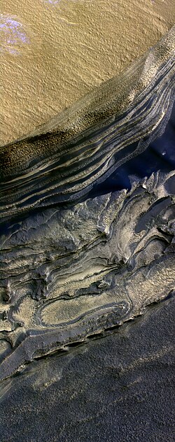 False color HiRISE image of a side of the Chasma Boreale, a canyon in the polar ice cap. Light browns are layers of surface dust greys and blues are layers of water and carbon dioxide ice. Regular geometric cracking is indicative of higher concentrations of water ice.