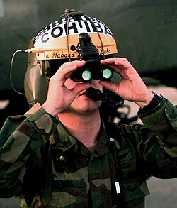Binocular night vision goggles on a flight helmet. The green color of the objective lenses is the reflection of the light interference filters, not a glow.