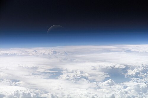 The atmospheric gases around Earth scatter blue light (shorter wavelengths) more than light toward the red end (longer wavelengths) of the visible spectrum; thus, a blue glow over the horizon is seen when observing Earth from outer space. The Moon is visible in the background.