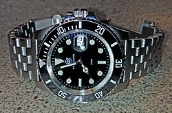 A watch with a date magnifying lens ("cyclops"). The cyclops is attached with transparent UV light curing adhesive to the top of the watch crystal.