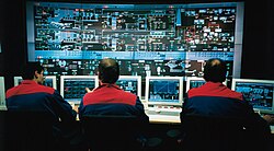 A modern control room where plant information and controls are displayed on computer graphics screens. The operators are seated as they can view and control any part of the process from their screens, whilst retaining a plant overview.