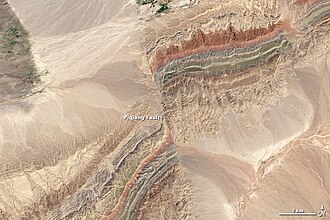 Satellite image of a fault in the Taklamakan Desert. The two colorful ridges (at bottom left and top right) used to form a single continuous line, but have been split apart by movement along the fault.