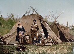 A Sami family in front of goahti. The tent in the background is a lavvu. Note the differences in the pole placement of the two structures. This photo was taken around 1900 in northern Scandinavia.