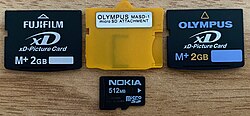 xD cards sold by FujiFilm and Olympus on either side of the Olympus MASD-1 xD to microSD adapter card (microSD card below for scale)