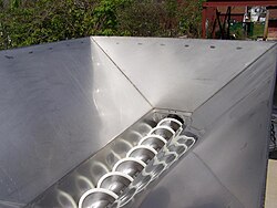 The corkscrew-shaped feed auger sits on top of a mechanical crusher-destemmer. Grape clusters are fed into the machine, where they are first crushed, then destemmed. Stems exit at the end, while juice, skins, seeds, and some debris exit the bottom.