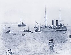 Komagata Maru (left background) being escorted by HMCS Rainbow and a swarm of small boats, 1914