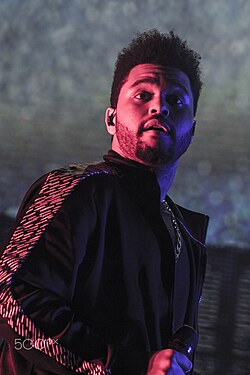 The Weeknd looks slightly up in a pink-lit environment during a concert
