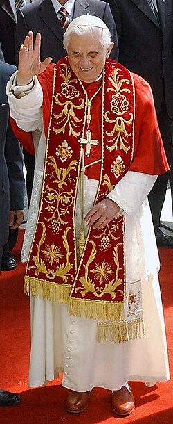 Benedict in choir dress with the red summer papal mozzetta, embroidered red stole, and the red papal shoes