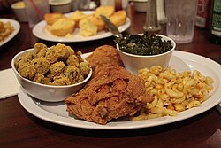 A traditional soul food dinner consisting of fried chicken with macaroni and cheese, collard greens, breaded fried okra, and cornbread