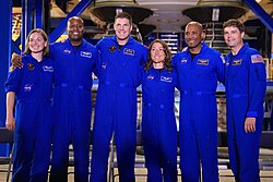 The backup (standing left) and prime crew of Artemis II after a news conference in December 2024. From left to right: Jenni Gibbons, Andre Douglas, Jeremy Hansen, Christina Koch, Victor Glover, Reid Wiseman