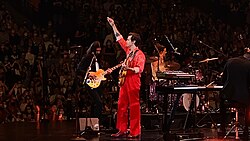 Harry Styles performing on stage, holding a guitar