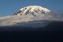 Snow-covered mountain rising above a coastline, viewed from the ocean