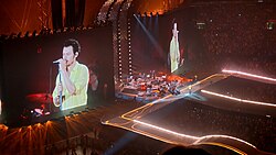 Harry Styles on a concert stage, surrounded by screens showing his performance