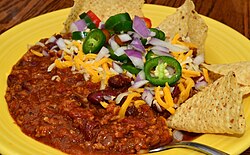 A bowl of chili served with traditional garnishes and tortilla chips