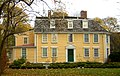 A large yellow colonial frame house with white trim. Additions expand the house to the left, and the roof has a few gabled dormers in it.