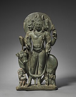 A c. 750–800 CE gray schist three-headed Shiva from Kashmir, with a three-eyed yogi-king front facing form, his consort Parvati as the left head, and three-eyed Bhairava as right head. His sons Ganesha and Kumara stand at his feet, and a three-eyed Vrishabha, his mount, stands behind.[151]