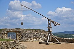 Photo of a reconstructed medieval trebuchet on a stone platform against a cloudy sky in the background