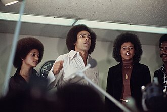 Newton (center) speaks to a crowd of Black Panthers at San Francisco International Airport with his wife Gwen (left) and Elaine Brown, July 5, 1977