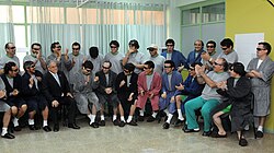 Color image of President Piñera visiting the rescued miners, who are dressed in hospital robes and pajamas while seated and standing in a semi-circle in a hospital room