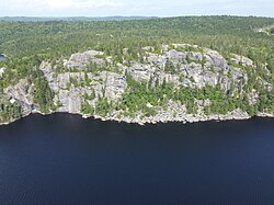 A tall cliff on the eastern shore of Paces Lake, Nova Scotia, with scree at its base. As the rate of erosion is quite slow, the scree has become partially forested.