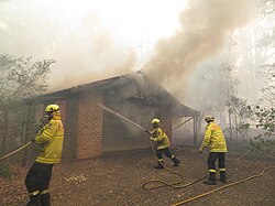 Firefighters work to save a burning house from an out-of-control bushfire in South West Sydney