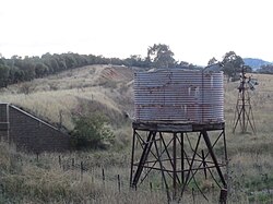 Derelict windmill connected to water pump with water storage tank in the foreground