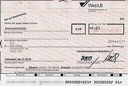 OCR-A on a German bank check. The ⑂, ⑀ and ⑁ characters are used to delimit particular fields in the machine-readable line (shown here partially pixelized out).