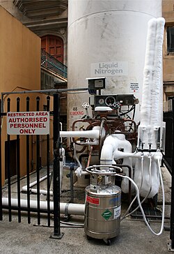 A medium-sized dewar is being filled with liquid nitrogen by a larger cryogenic storage tank.