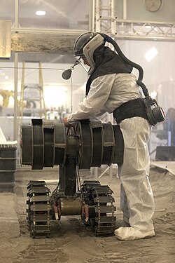Person in protective gear working in the regolith bin of Swamp Works at NASA's Kennedy Space Center (Florida), testing the Regolith Advanced Surface Systems Operations Robot (RASSOR)