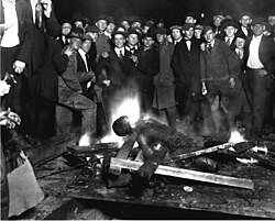 A group of White men pose for a 1919 photograph as they stand over the Black victim, Will Brown, who had been lynched and had his body mutilated and burned during the Omaha race riot of 1919 in Omaha, Nebraska. Postcards and photographs of lynchings were popular souvenirs in the US.[70]