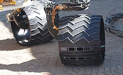 Wheels of a working sibling to Curiosity. The Morse code pattern (for "JPL") is represented by small (dot) and large (dash) holes in three horizontal lines on the wheels. The code on each line is read from right to left.
