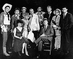 Guest stars for the 1961 premiere episode of The Dick Powell Show, "Who Killed Julie Greer?". Standing, from left: Ronald Reagan, Nick Adams, Lloyd Bridges, Mickey Rooney, Edgar Bergen, Jack Carson, Ralph Bellamy, Kay Thompson, Dean Jones. Seated, from left, Carolyn Jones and Dick Powell.