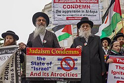 Members of Neturei Karta holding Palestinian flags and placards saying that "Judaism condemns the state of Israel and its atrocities" in London, 2022