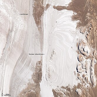 The dry lakebeds and yardangs in Salar de Arizaro, imaged by NASA's Earth Observing-1 satellite. In the upper left corner, small rounded bumps in the landscape are yardangs, dusty hills formed when soft rocks are weathered and abraded by winds. The yardangs are aligned precisely with the northwesterly winds. On the right, bulbous hills have sharps edges, a formation typical of salt weathering around the base. During salt weathering, rocks are eroded by repeated salt crystal growth. The eroded material has been blown away by the strong winds of the high desert, leaving the sharp edge.[2]