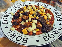 Plate of chili con carne served Tex-Mex style, topped with pork, beef, cheddar, and monterey jack