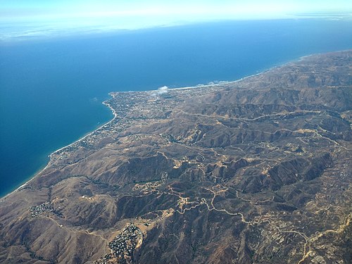 Malibu, California aerial view in July 2021 showing residential development deep in the mountains. Note previously burned area (darker areas) on mountains.