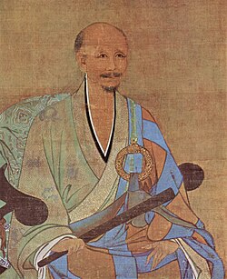 A portrait of an older, balding man in a half pale green and half sky blue robe. He is sitting on an armchair holding a thin wooden stick, possibly a folded up fan.