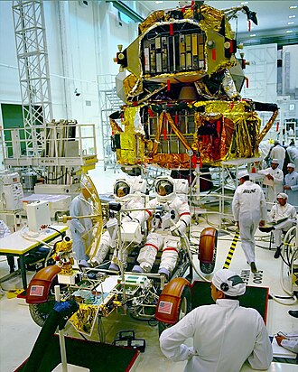 Schmitt, (left), Cernan, (right) in a training LRV, with the Lunar Landing Module in the background.