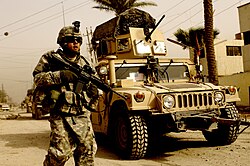 A U.S. soldier on patrol in Iraq with the support of a Humvee vehicle